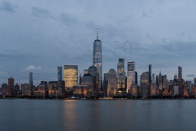 Illuminated buildings in city against cloudy sky