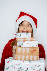 Portrait of smiling woman holding christmas gifts while standing against white background