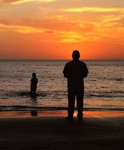 Rear view of silhouette man standing on beach during sunset