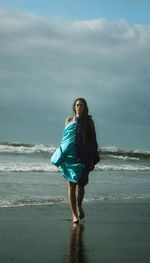 Portrait of young woman standing at beach against sky