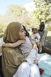 Woman wearing headscarf embracing daughter at park