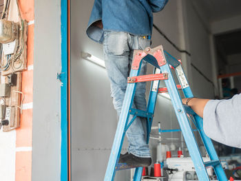 Low section of man standing on ladder in workshop