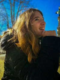 Smiling young woman looking away while sitting in park during winter