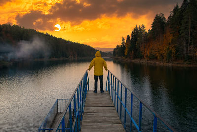 Silhouette man walking on pier over lake against sky during sunset