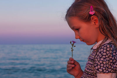 Adorable little girl looks on flower on beach.cute child with wet long hair in dress smelling flower