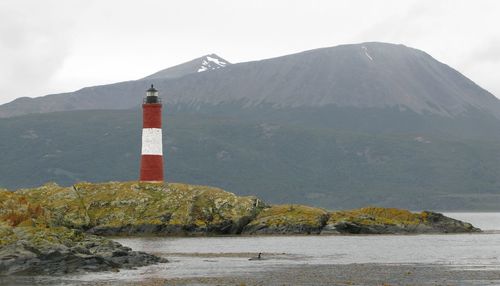 Lighthouse amidst buildings and mountains against sky