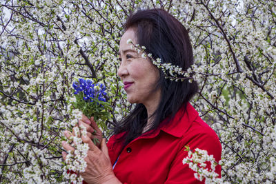 Portrait of young woman with red flowers against trees