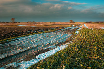 Snow on a dirt road, horizon and dark cloud on the sky, fields and rural view