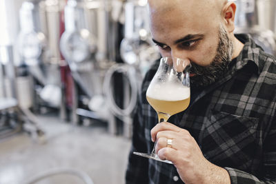Close-up of male worker examining craft beer while standing at factory