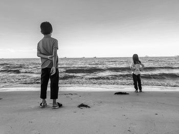 Rear view of kids standing at beach against sky