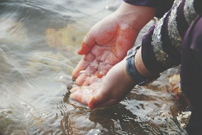 Midsection of woman cupping hands on water in lake