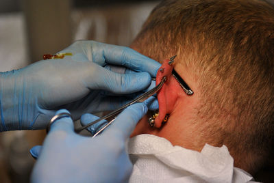 Cropped hands piercing ear of man