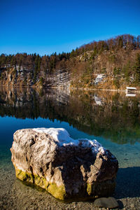 Rocks by lake against clear blue sky