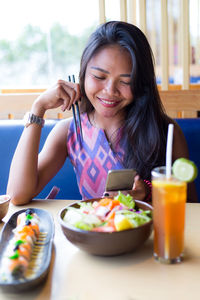 Close-up of a smiling young woman using phone in restaurant