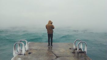 Rear view full length of man standing on pier by sea during foggy weather