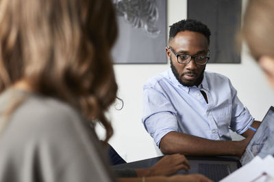 Colleagues discussing over laptop computer while sitting in conference room