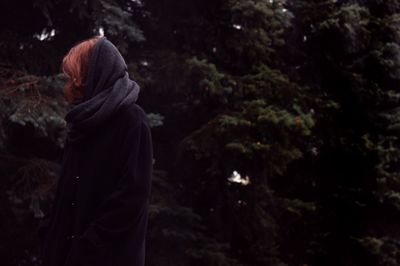 Side view of woman standing against trees during winter