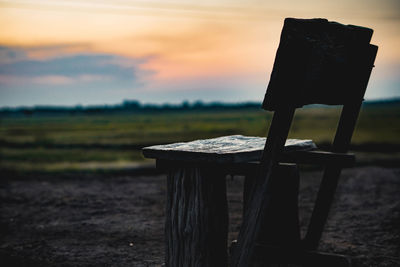 Empty wooden chairs on field against sky during sunset