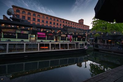 Bridge over canal by buildings in city at dusk