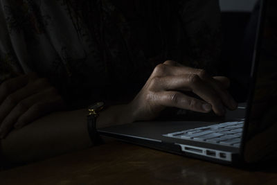 Close-up of hand using laptop in darkroom