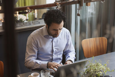 Businessman working on laptop in creative office seen through glass