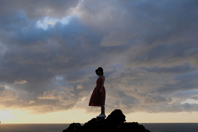 Rear view of woman standing on beach against sky