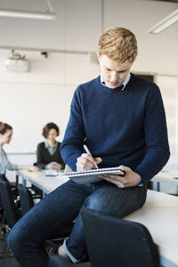 Young boy writing in notepad while sitting on table