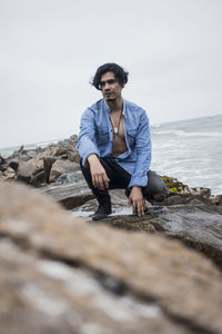 Portrait of young man standing on rock by sea