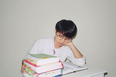 Portrait of young woman reading book against wall