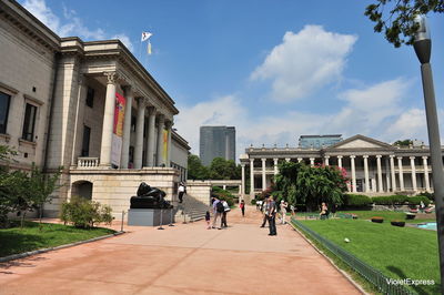 People walking by buildings in city against sky