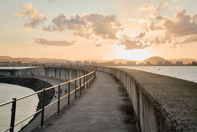 Footpath by sea against sky during sunset