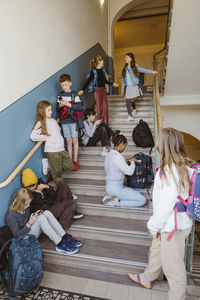 Male and female students using smart phones on steps on school building
