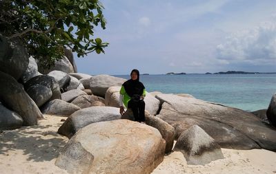 Man sitting on rock by sea against sky