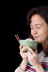 Portrait of smiling woman holding ice cream against black background