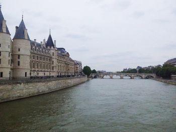 View of buildings by river against cloudy sky