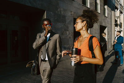 Male entrepreneur drinking coffee while discussing with female colleague on footpath in city