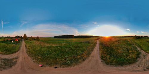 Panoramic shot of road amidst field against sky during sunset