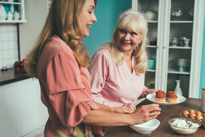 Cheerful daughter and mother preparing muffins at kitchen