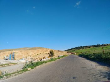 Road amidst land against clear blue sky