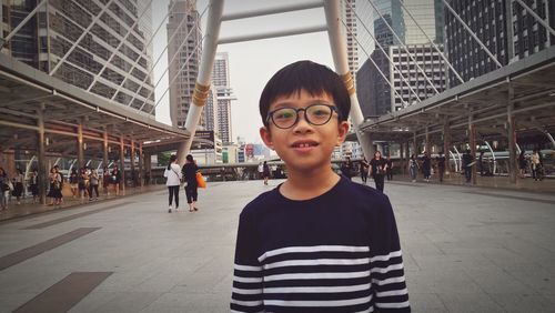 Portrait of boy standing on footpath in city