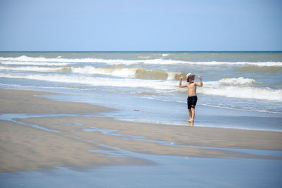 Rear view of a boy on beach against sky