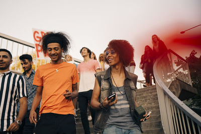 Smiling friends with banner talking while walking on steps against sky