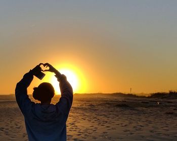 Man holding camera on beach against clear sky during sunset