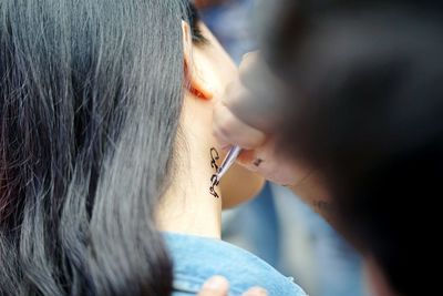 Cropped hand applying henna tattoo on woman neck