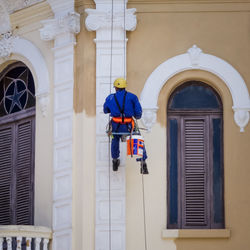 Rear view full length of painter hanging on ropes while painting building