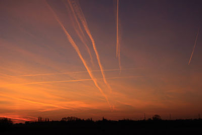 Low angle view of vapor trails in sky at sunset