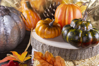 Small pumpkins, pinecones, and squash on wood stacked on leaf-covered hay with a golden background
