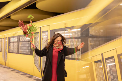 Woman holding bouquet with scarf covering face standing against subway train