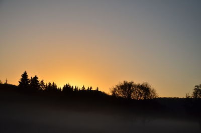 Silhouette trees on landscape against clear sky at sunset