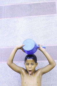 Shirtless boy pouring water on himself against wall